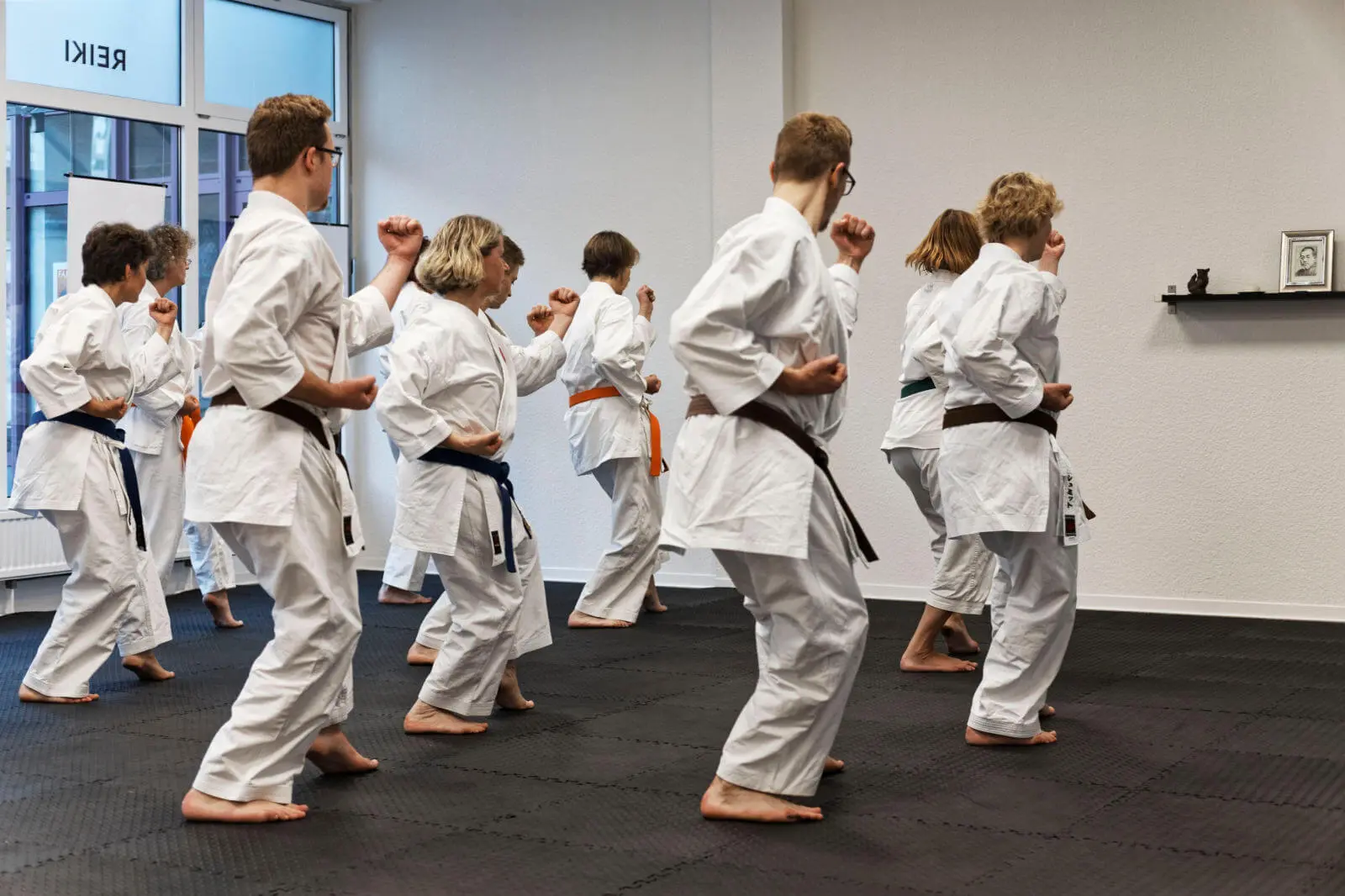 Zehn Menschen stehen im Karateanzug auf einer Trainingsfläche und üben Kata